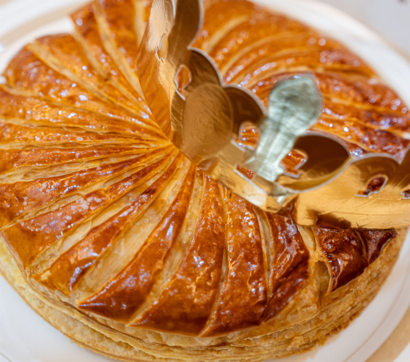 Une magnifique galette des rois dorée et feuilletée avec une fève et une couronne dorée, symbolisant la fête en janvier